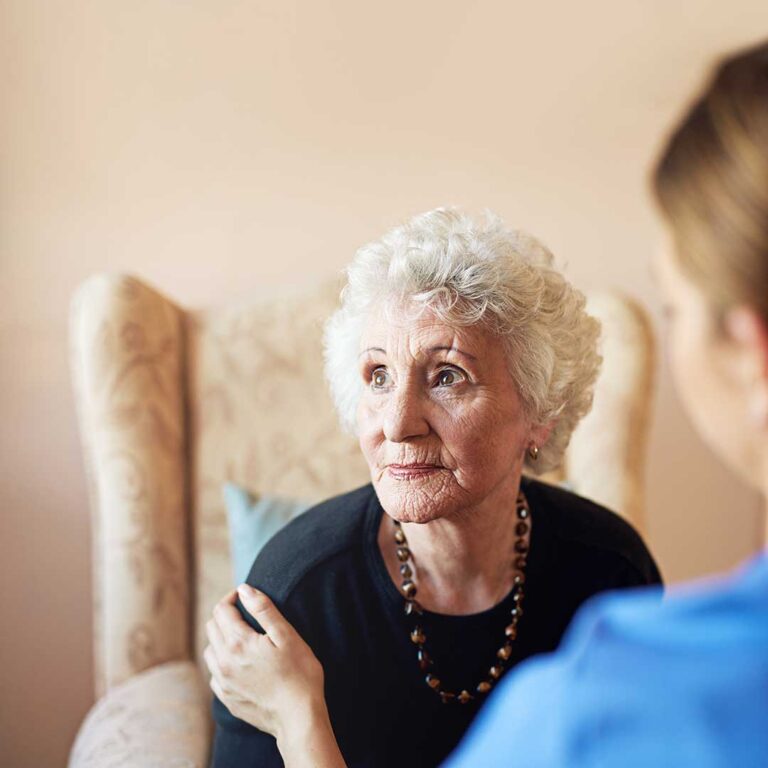 A caregiver assisting an older resident with a daily activity in a residential living area.
